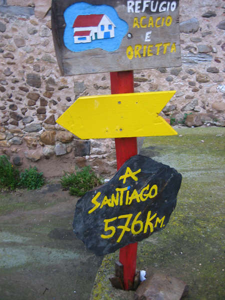 Wegweiser am Camino bei Redecilla: gelber Pfeil, Herbergsschild und Schiefertafel „A Santiago 576 km“